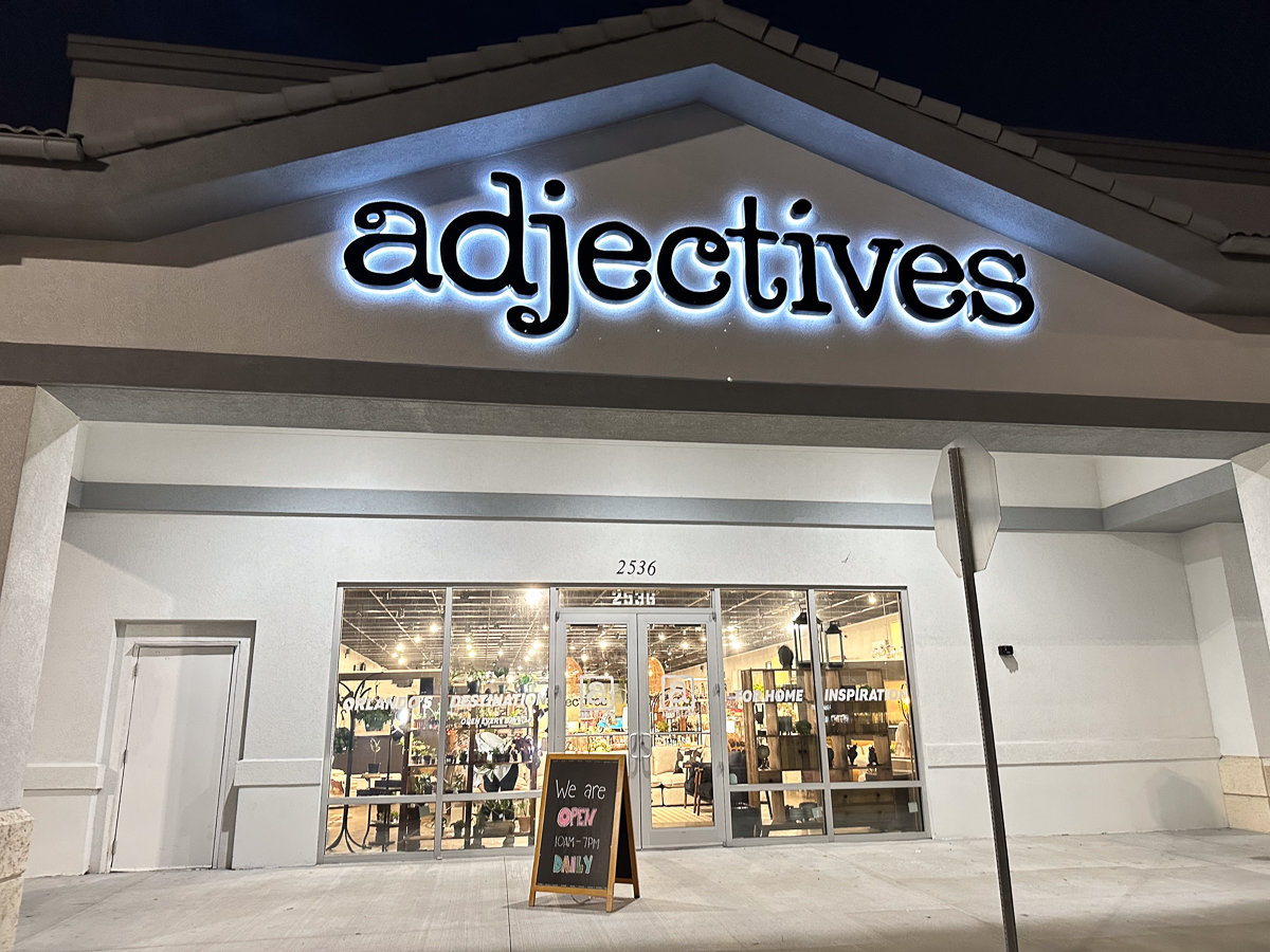 front of adjectives shop with black sign lit in blue